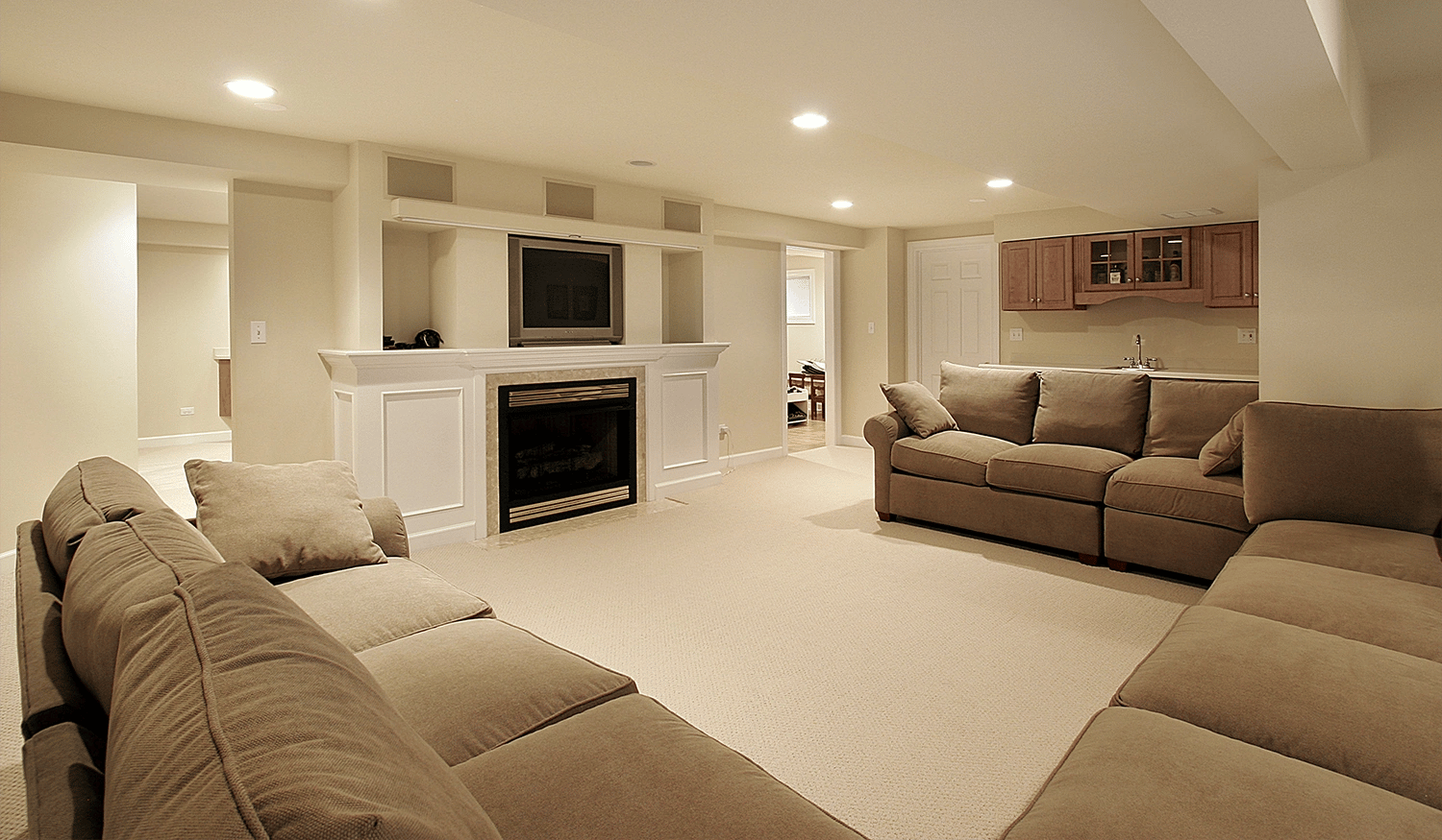 A basement remodeled as an entertainment room. Three large brown couches in front of a fireplace and television.