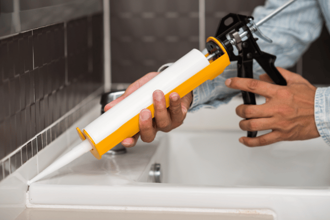 DIYer applying silicone sealant to the back edge of a sink