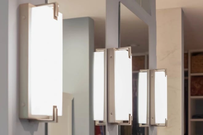 A close up of side-mounted wall sconces next to two vanity mirrors