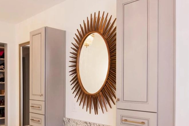 A fancy framed mirror in a bathroom between two storage towers