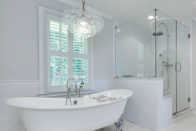 A freestanding tub next to a window treatment of shutters