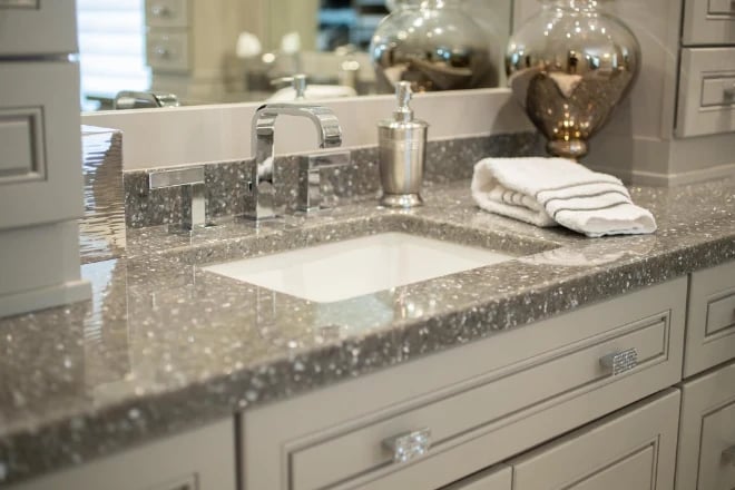 A gray-colored speckled countertop material surrounding a sink on a bathroom vanity 
