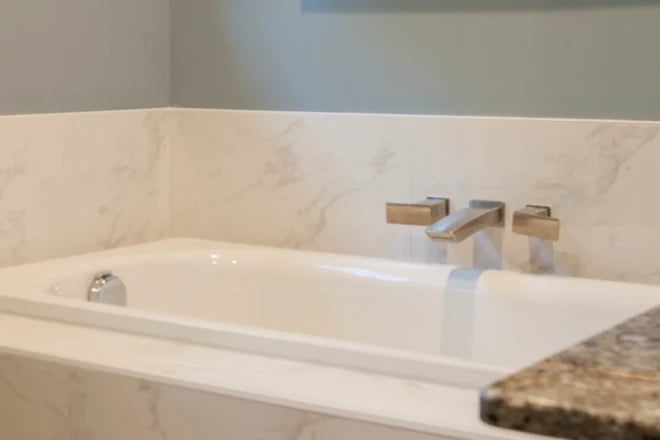 A wall-mounted bathroom faucet with a marble backsplash
