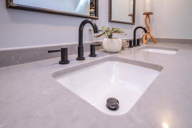 An engineered stone (quartz) bathroom countertop material surrounds the double sinks on this bathroom vanity