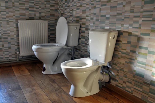 Two toilets, one comfort height, the other standard height, sit next to each other in a bathroom