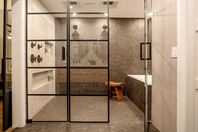 A large walk in shower with a mix of different size tiles that are approximately the same color.