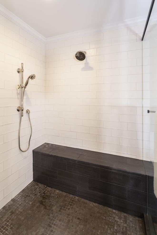 A black tile bench and floor in a shower with white tile walls.