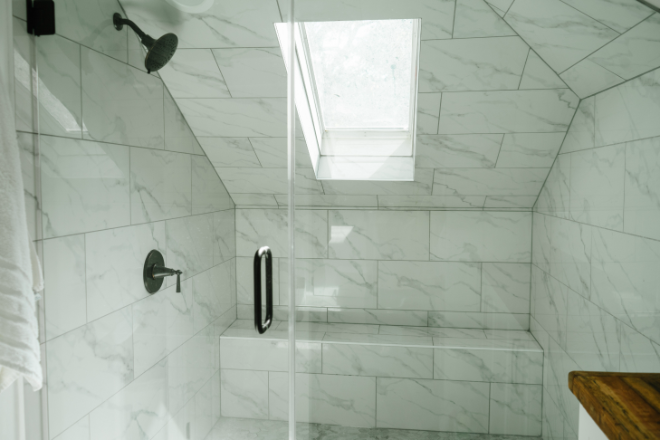 A glass enclosed shower with a skylight and large tiles