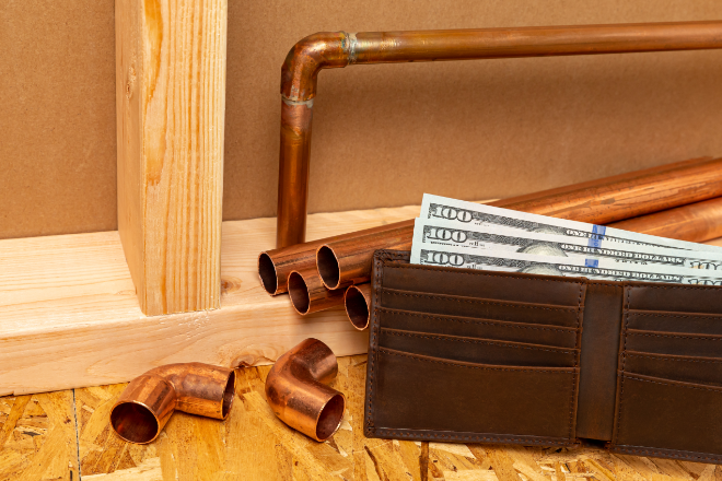 A wallet with money infront of wooden framing and copper piping pieces