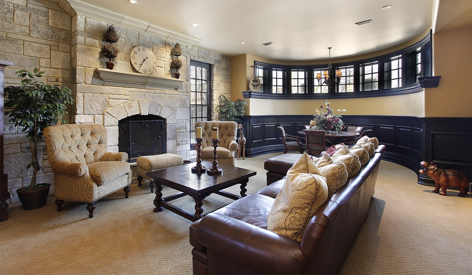 A remodeled basement featuring a dark leather couch, stone fireplace, and several armchairs.