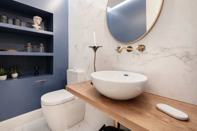 Designer toilet with half circle porcelain sink on light wood countertop and ornate shelving on blue wall
